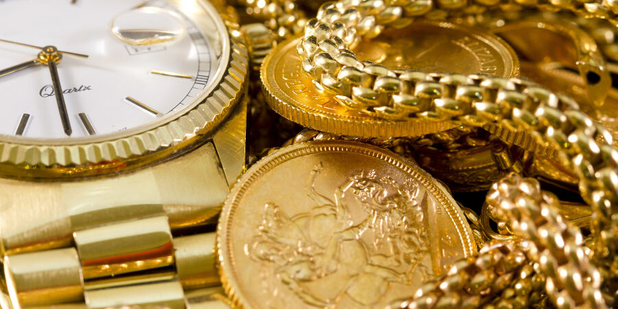 A golden watch, golden chains and a golden bullion coin on display.